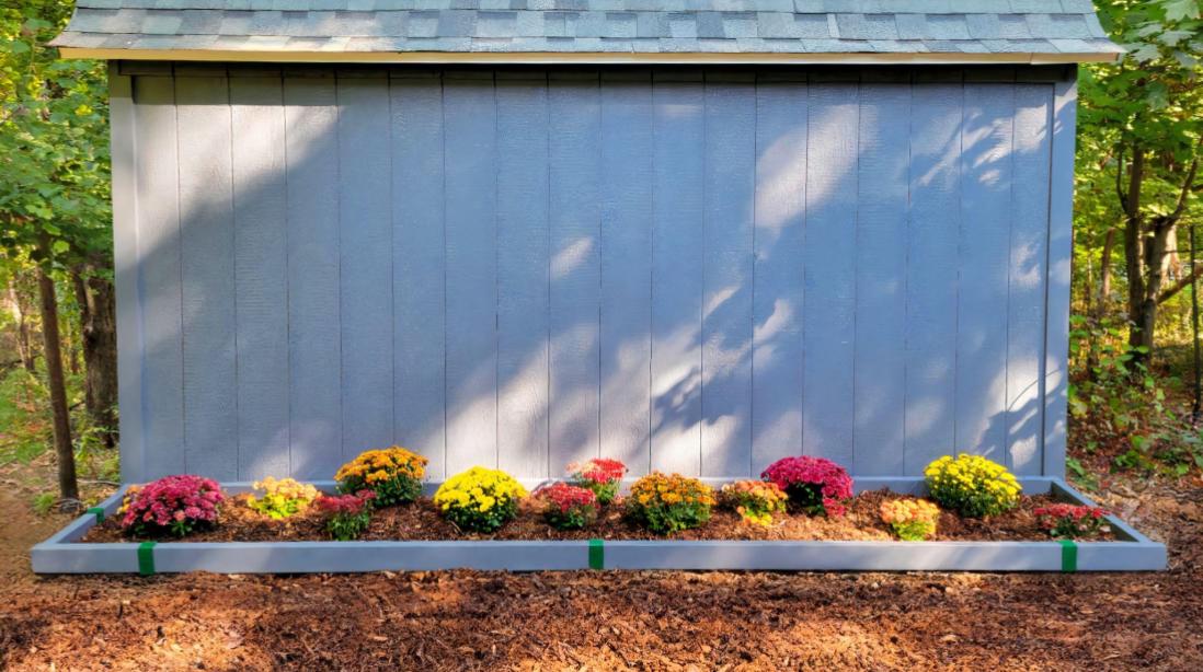 A flower bed installed on the side of a shed edged with painted 2x4 lumber and Forest Green 2xEDGE Staples.