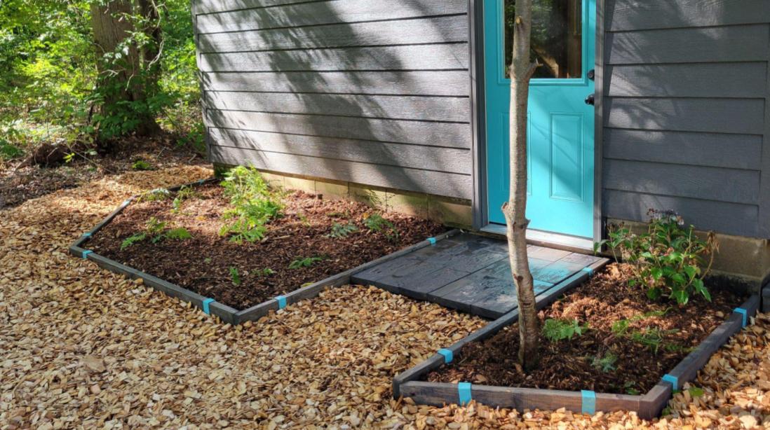 Photo of an entryway with garden beds edged with 2x4 lumber stained dark walnut and Robins Egg Blue 2xEDGE Staples.