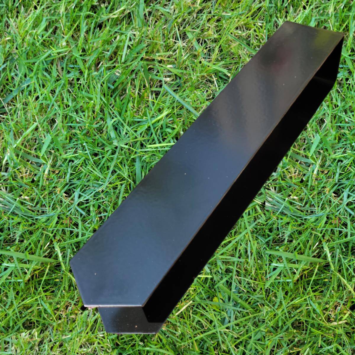 A close-up shot of a 2xEDGE Satin Black Staple lying on a patch of lawn.