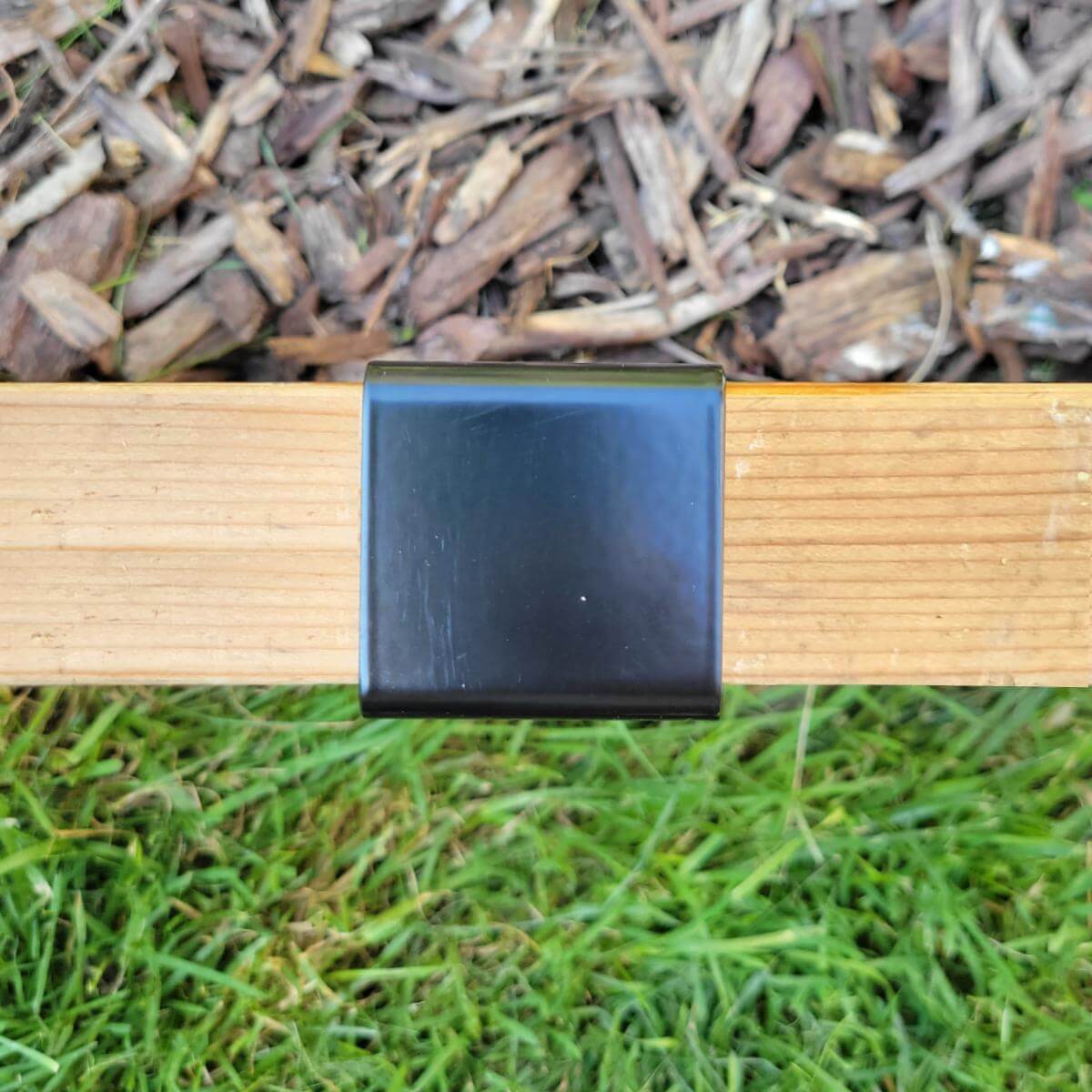 Closeup of top of 2xEDGE Satin Black Staple installed on two-by lumber with mulch on one side and grass on the other.