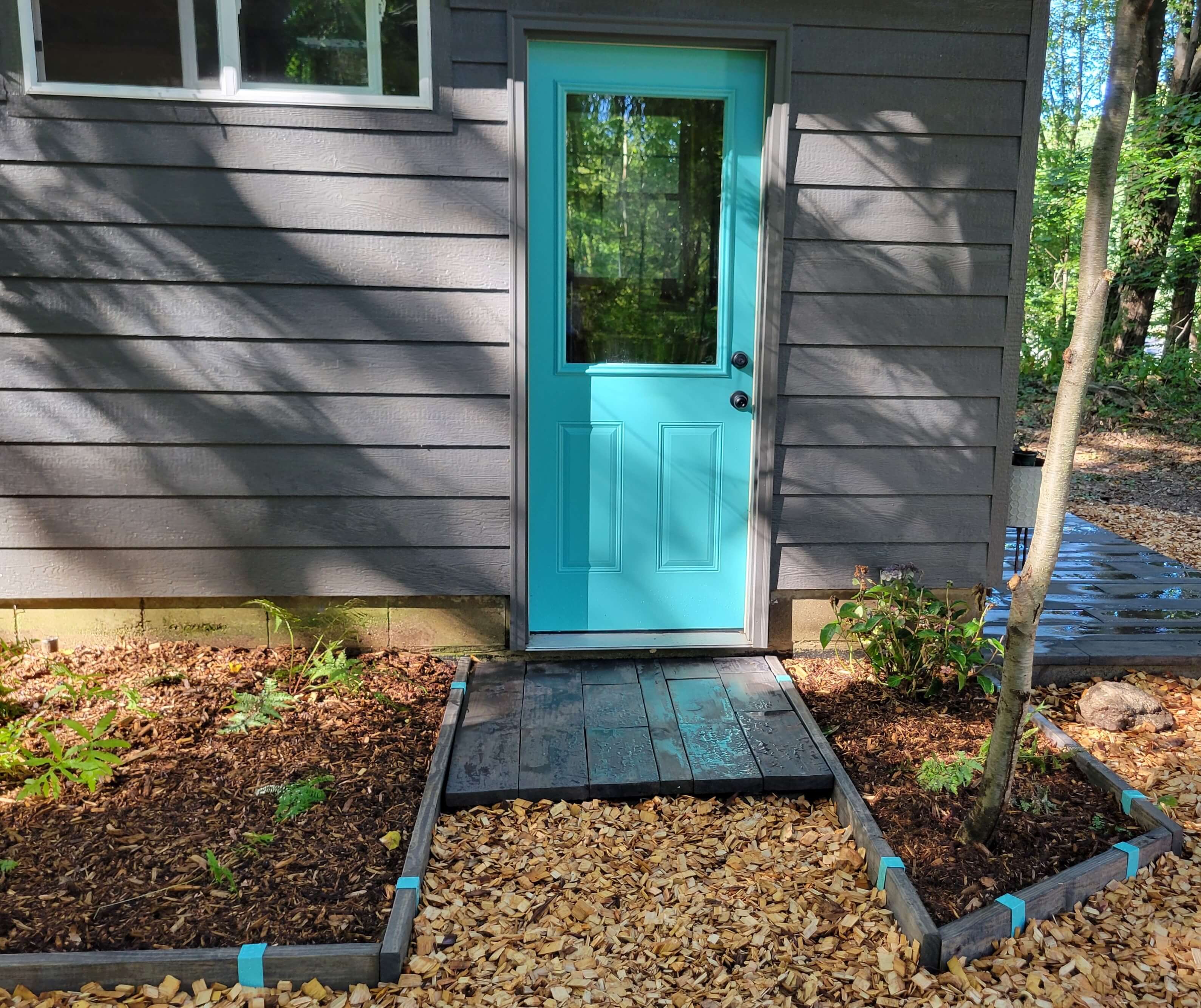 Wooden garden edging stained a dark walnut and installed with contrasting Robins Egg Blue 2xEDGE Staples around an entryway garden.