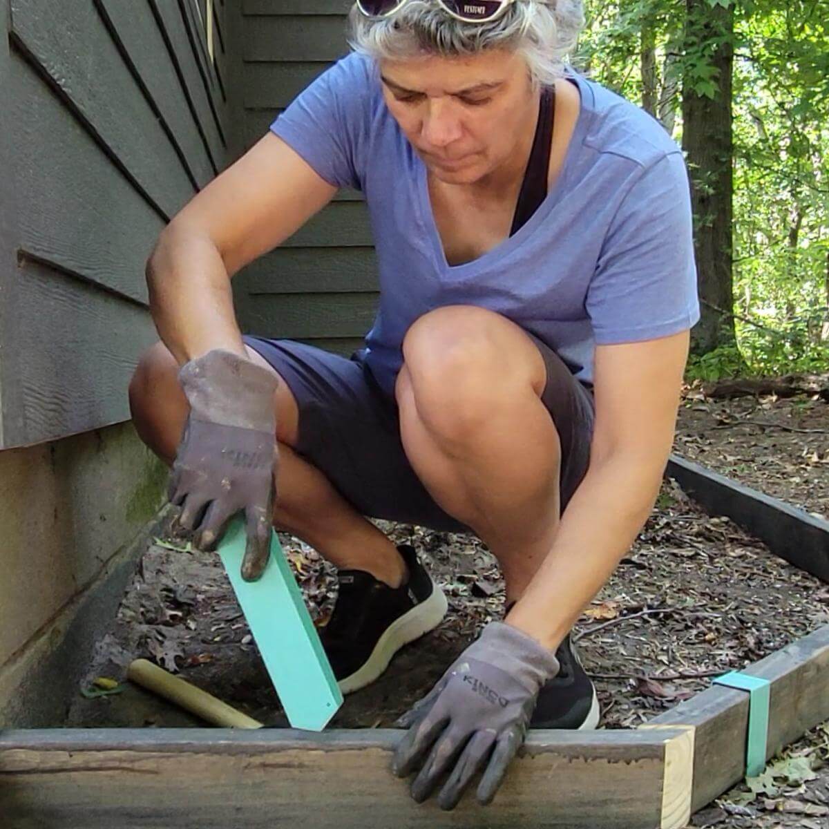 2xEDGE Staples creator Lisa Brooks preparing to install a Robins Egg Blue 2xEDGE Staple on a piece of stained pressure treated 2x4 lumber to create flower bed edging.
