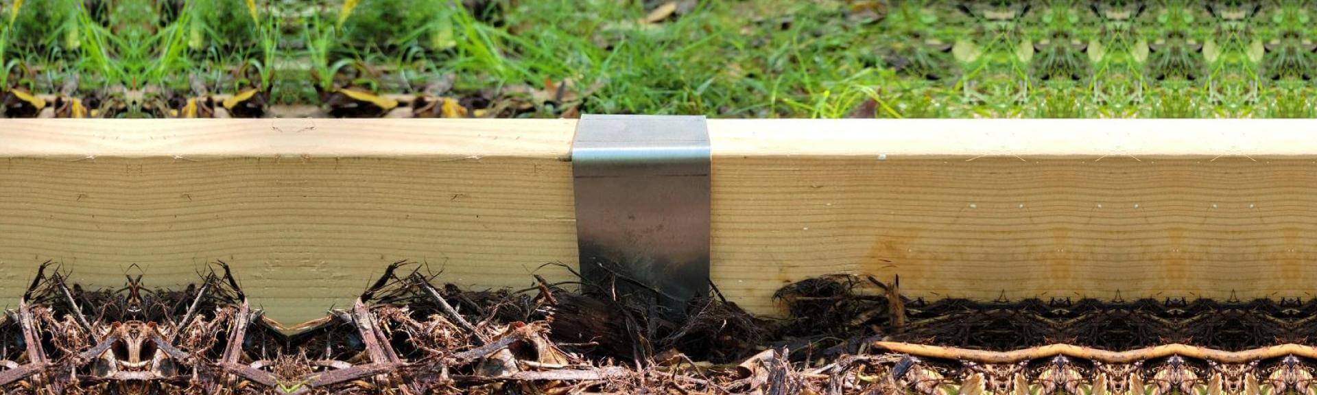 Long length of pressure treated lumber installed with rustic steel 2xEDGE Staple to separate lawn and mulch.