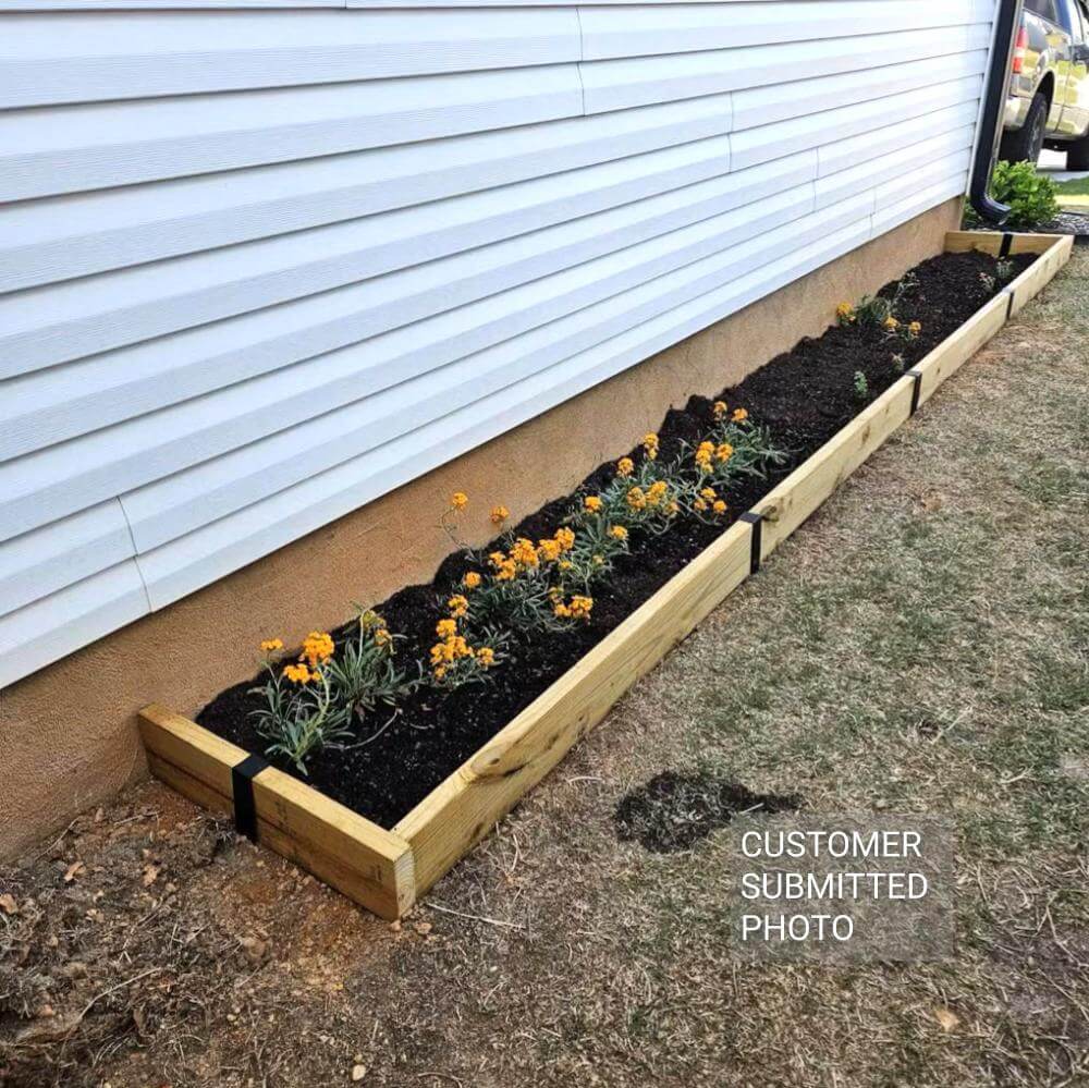 A long and narrow flower bed next to a house created with 2x6 lumber and Satin Black 2xEDGE Staples.