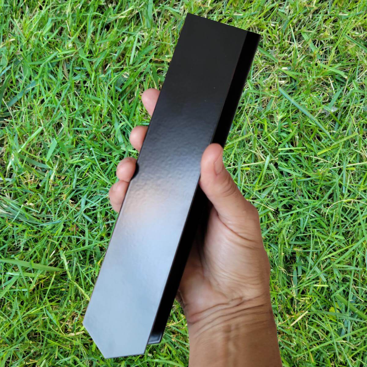 Closeup of a 2xEDGE Satin Black Staple being held in the air with lawn in the background.