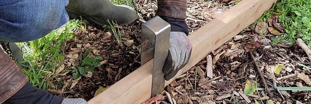 2x4 lumber placed on the ground in a perpendicular position and a 2xEDGE Staple placed over the lumber in preparation to install the lumber as landscape edging.