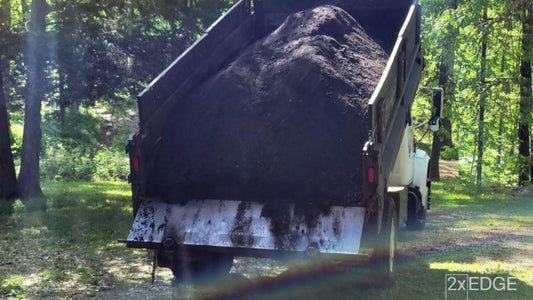 A dump truck unloading mulch onto a driveway with a rainbow in the forefront.