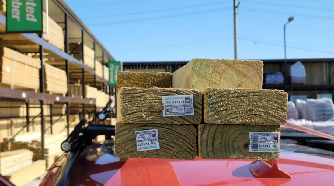 2x4 lumber strapped to the roof of a car parked in a lumber yard.