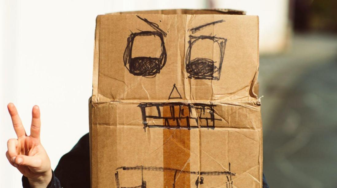 A person wearing a mask made out of a cardboard box with a face drawn on it.