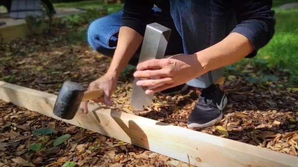 A person placing a 2xEDGE Staple on a 2x4 in preparation to install it with a rubber mallet