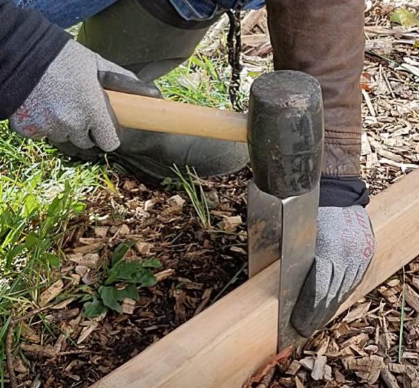 A person striking the top of a 2xEDGE Staple with a mallet to install 2x4 lumber as landscape edging.