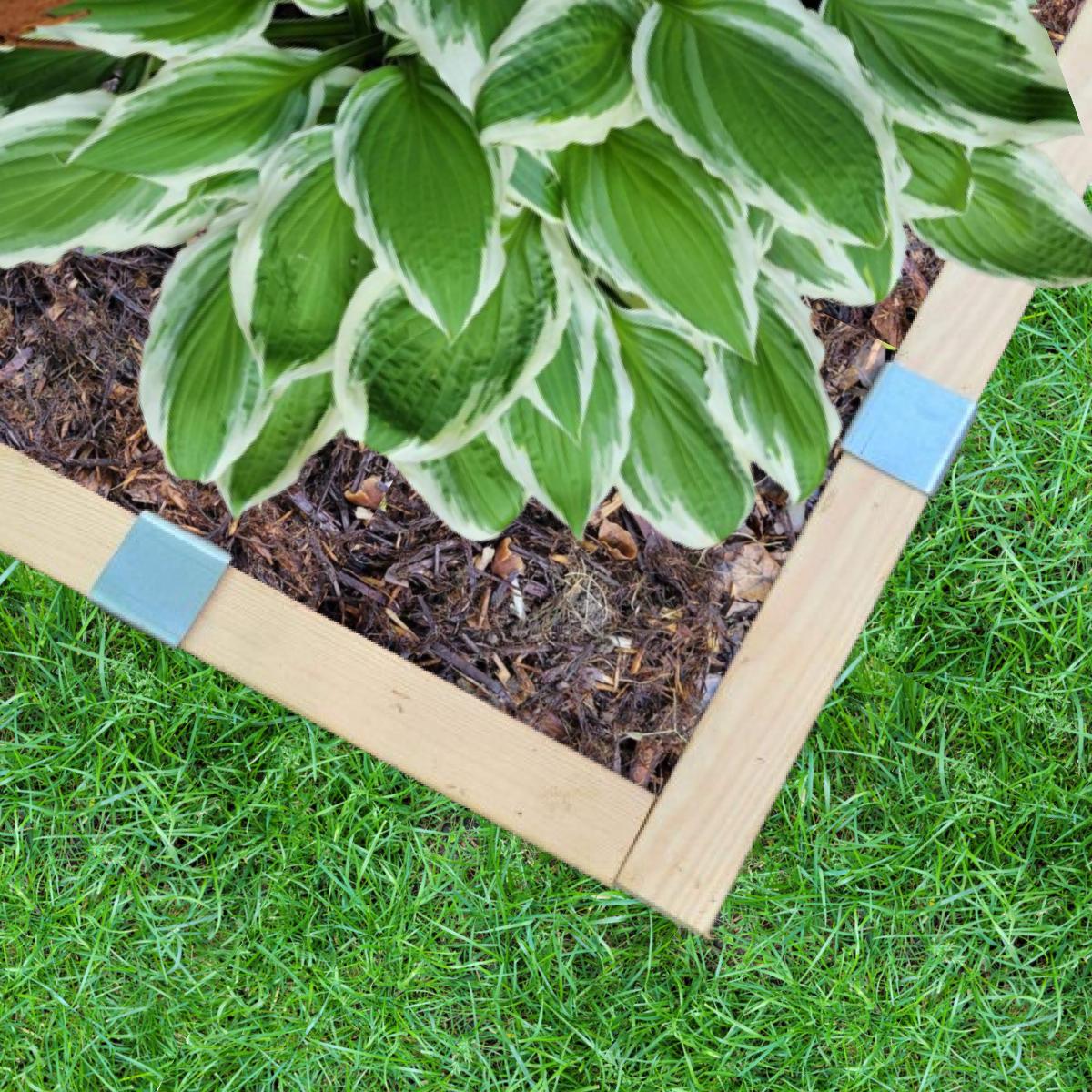 A photo of two 2x4s meeting at a corner, held in place with 2xEDGE staples, with mulch, grass, and a hosta