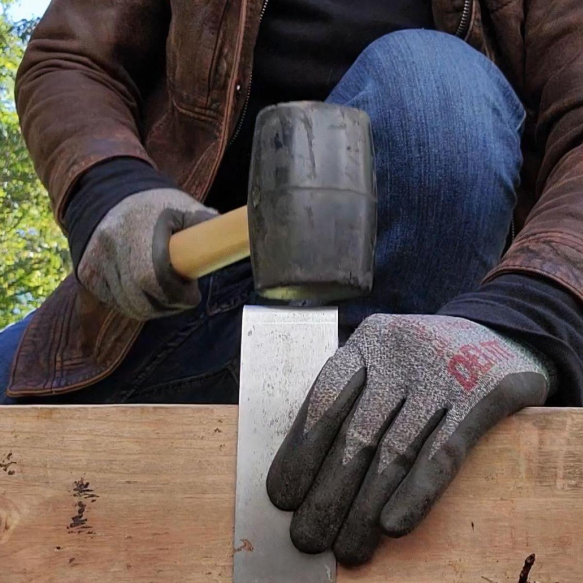 A person wearing a leather work jacket and gloves using a rubber mallet to tap a 2xEDGE Staple in place, securing 2x4 lumber to the ground to serve as landscape edging.