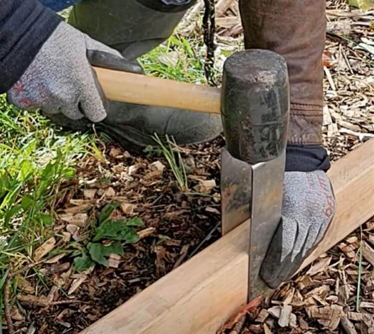 Installer holding a rubber mallet as it strikes the top of a 2xEDGE Staple to secure 2x4 lumber to the ground.