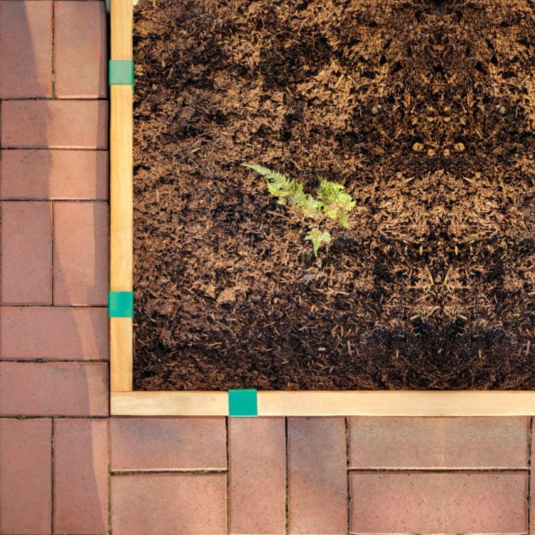 Garden bed next to a red brick patio separated by 2x4 lumber installed with Forest Green 2xEDGE Staples to seve as garden edging.