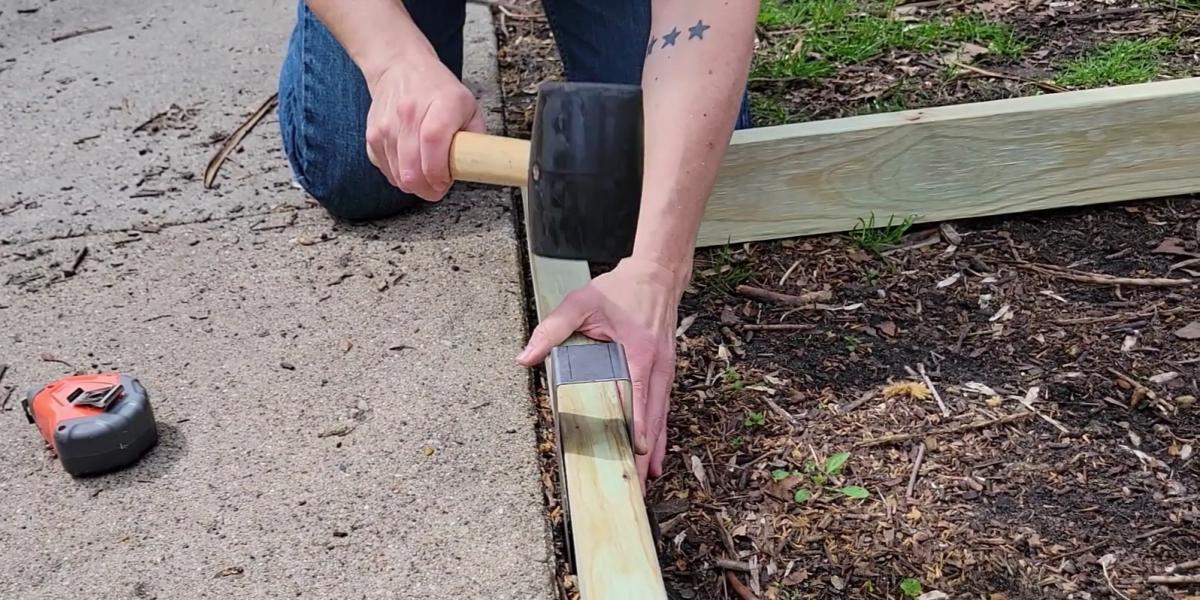 Someone installing a 2x4 with a 2xEDGE Staple to create wooden curb strip landscape edging.
