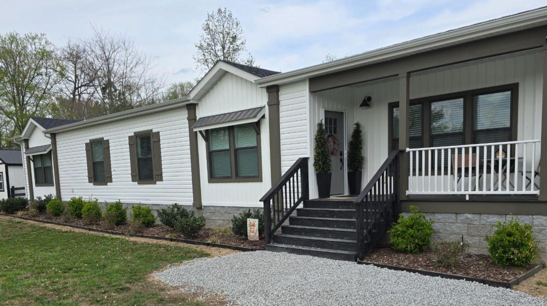 A house with white exterior and dark brown trim and dark walnut landscape edging separating a gravel walkway and lawn from front of house garden beds.