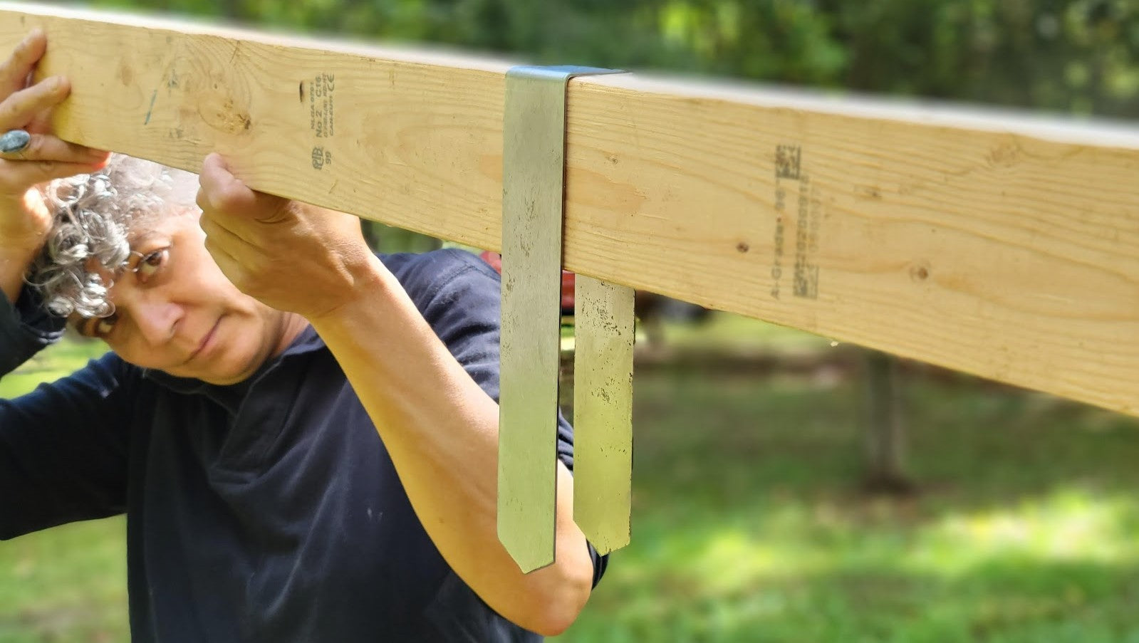 Person holding a 2x4 in the air with a 2xEDGE Staple hanging from it to illustrate how the staples wrap around lumber