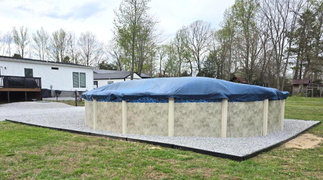 An above ground swimming pool installed on a gravel bed edged with dark walnut 2x lumber edging.